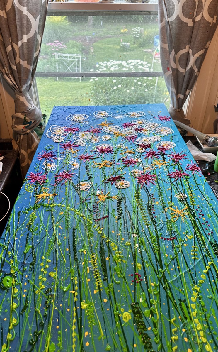 A painting of a meadow: green stems and grasses rising through a blue field, with magenta, yellow, and white painted blooms.